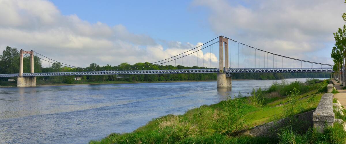 A suspension bridge over a river with greenery and trees in the background.