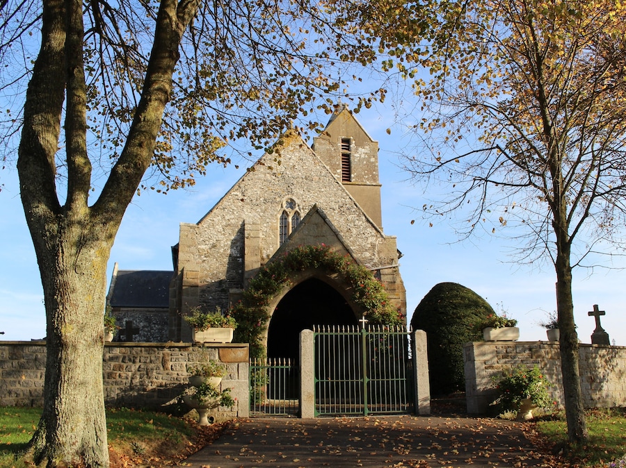 Una iglesia de piedra con una entrada de arco apuntado, una torre de campanas y una cruz en la entrada.