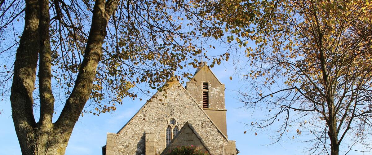 A stone church with a pointed arch entrance, a bell tower, and a cross at the entrance.