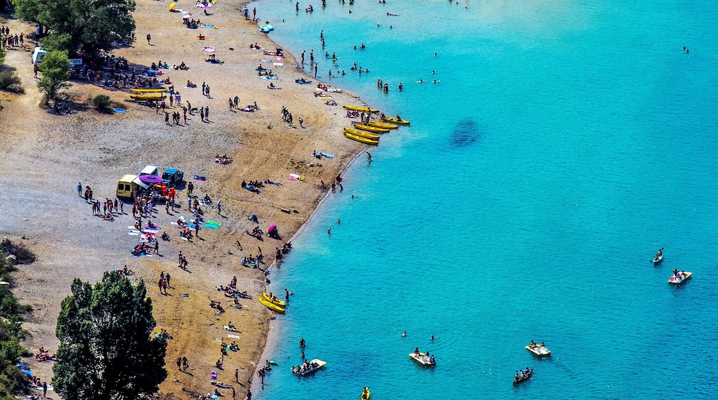 Una zona costera con playa arenosa, aguas turquesas cristalinas y numerosos barcos.