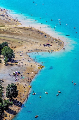 Una zona costera con playa arenosa, aguas turquesas cristalinas y numerosos barcos.