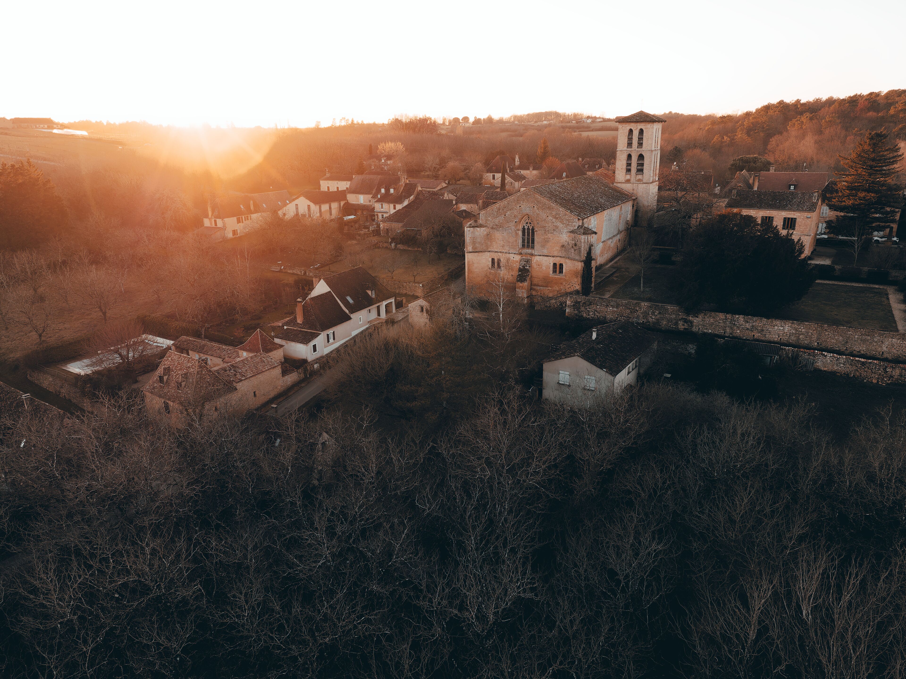 An aerial view of a historic village with a prominent church and tower, surrounded by trees and open fields.