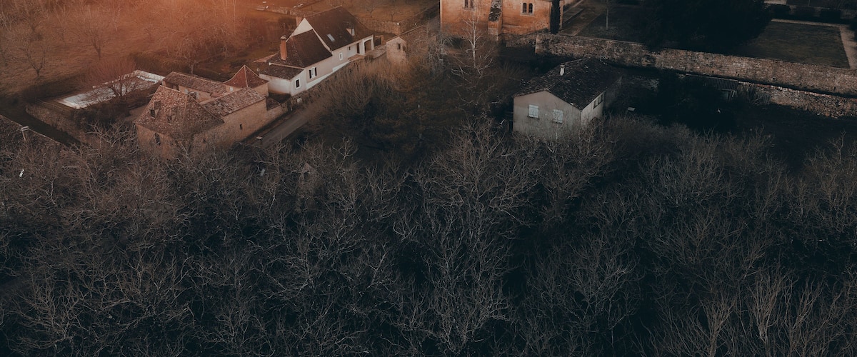 An aerial view of a historic village with a prominent church and tower, surrounded by trees and open fields.