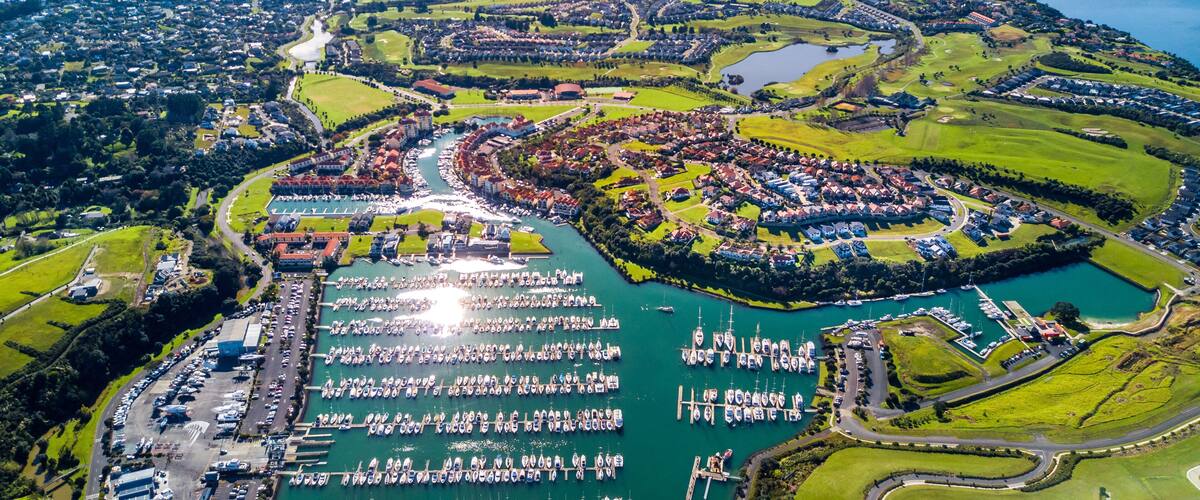 An aerial view of a coastal town with a marina, green hills, and a large body of water.