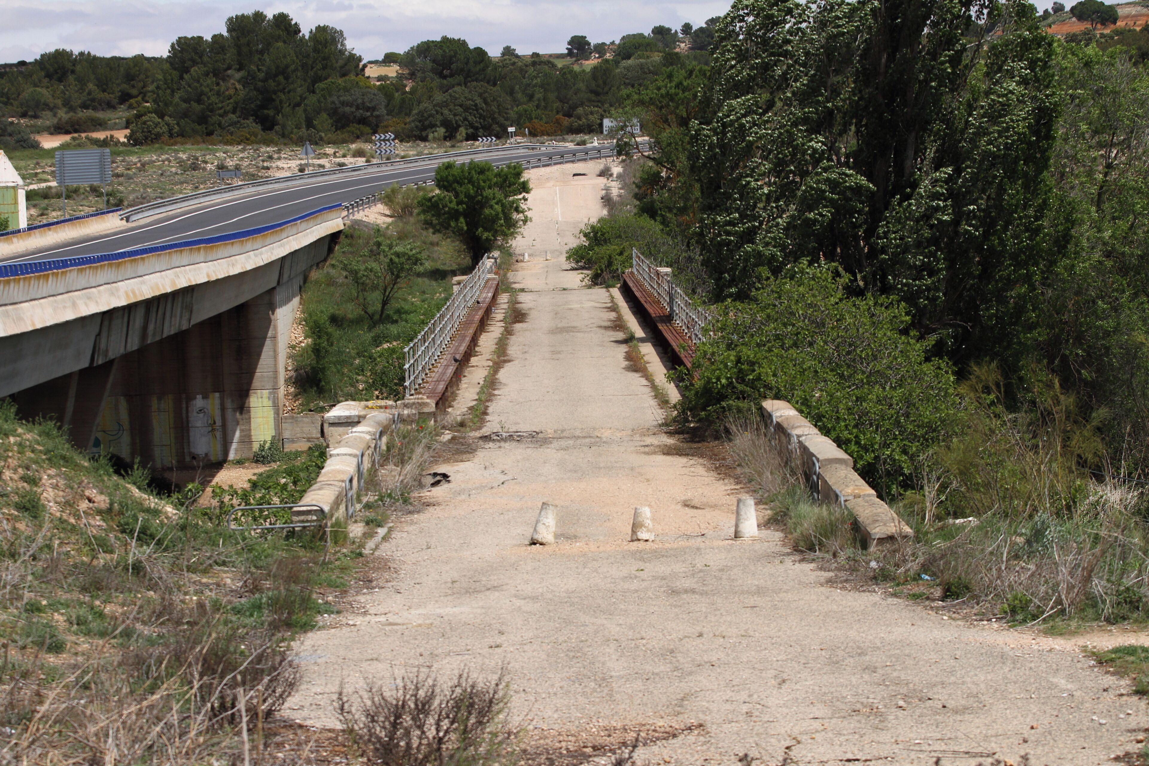 A bridge over a dirt road with a highway in the background.