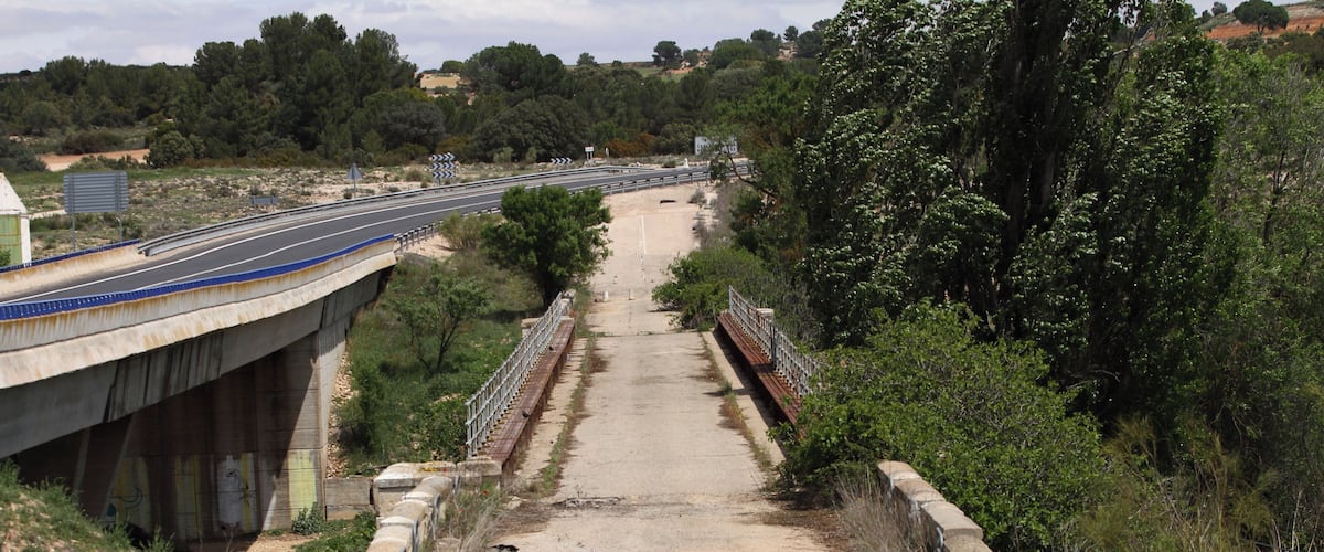 A bridge over a dirt road with a highway in the background.