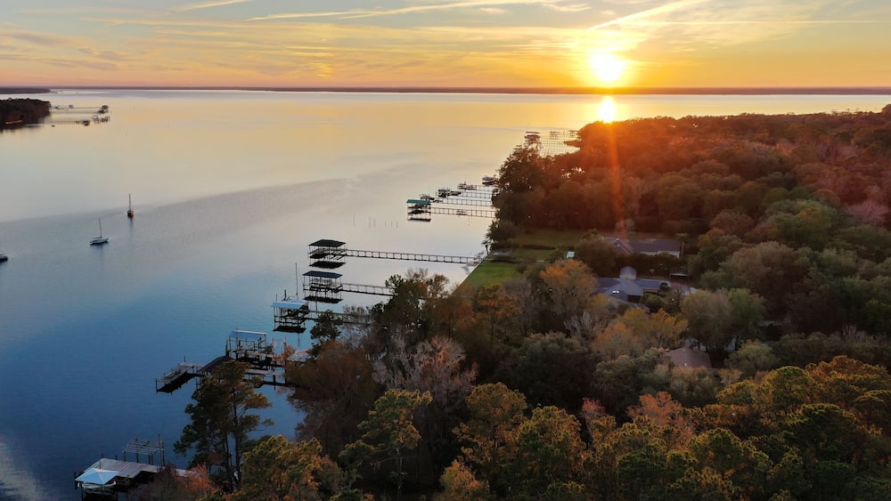 Un coucher de soleil sur un lac paisible, avec des quais et des arbres environnants.