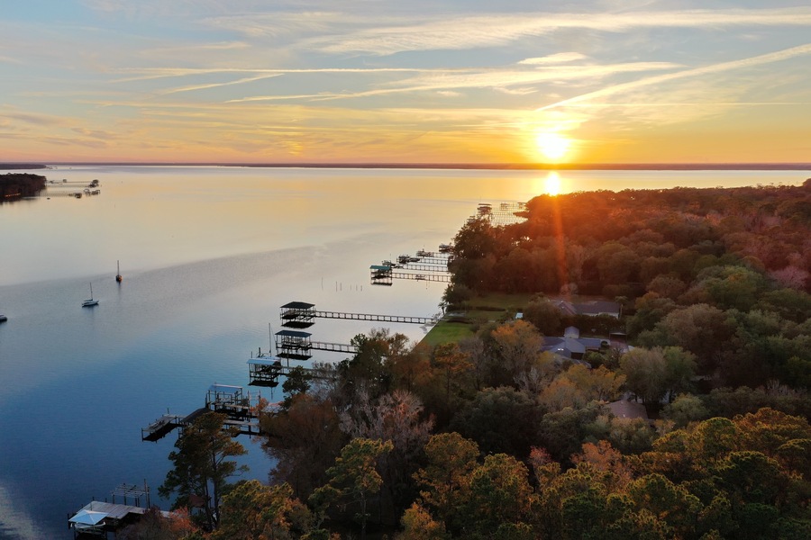 A sunset over a calm lake with dock structures and surrounding trees.