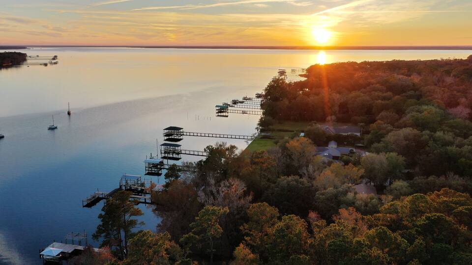 A sunset over a calm lake with dock structures and surrounding trees.