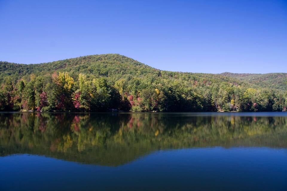 Um lago calmo refletindo um morro arborizado com folhagem outonal.