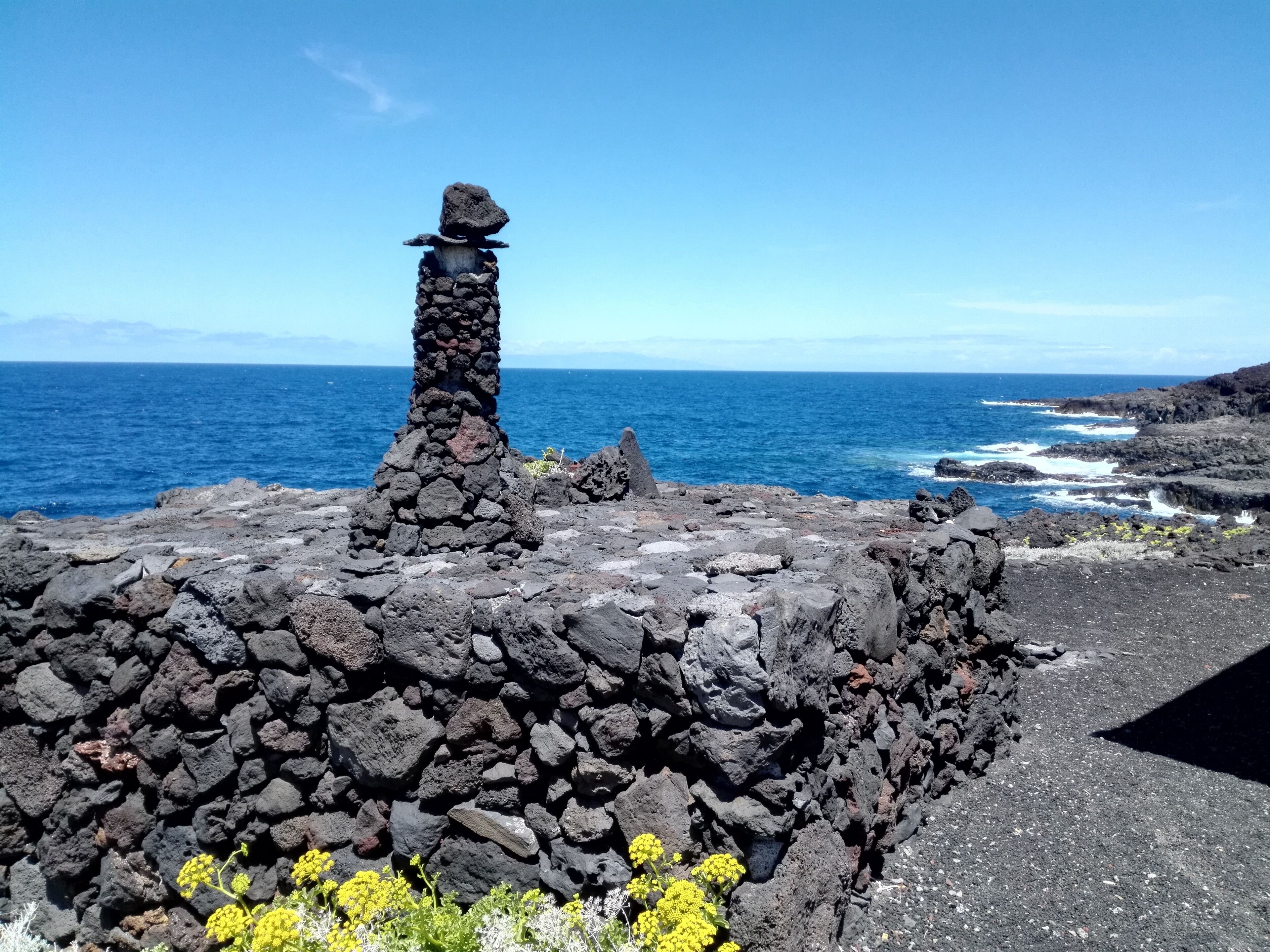 A rocky coastal landscape with a prominent stone structure and the ocean in the background.