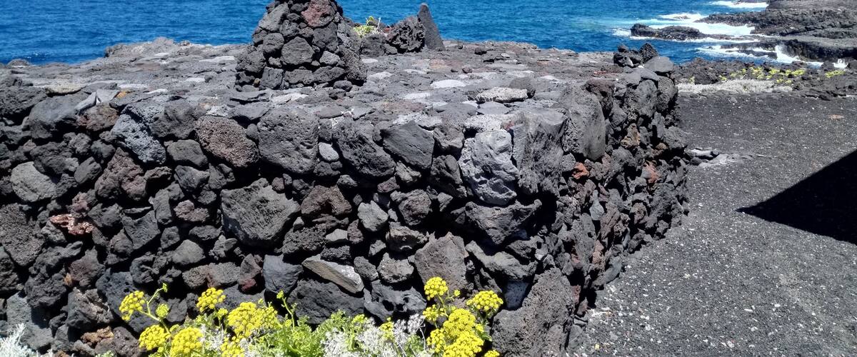 A rocky coastal landscape with a prominent stone structure and the ocean in the background.