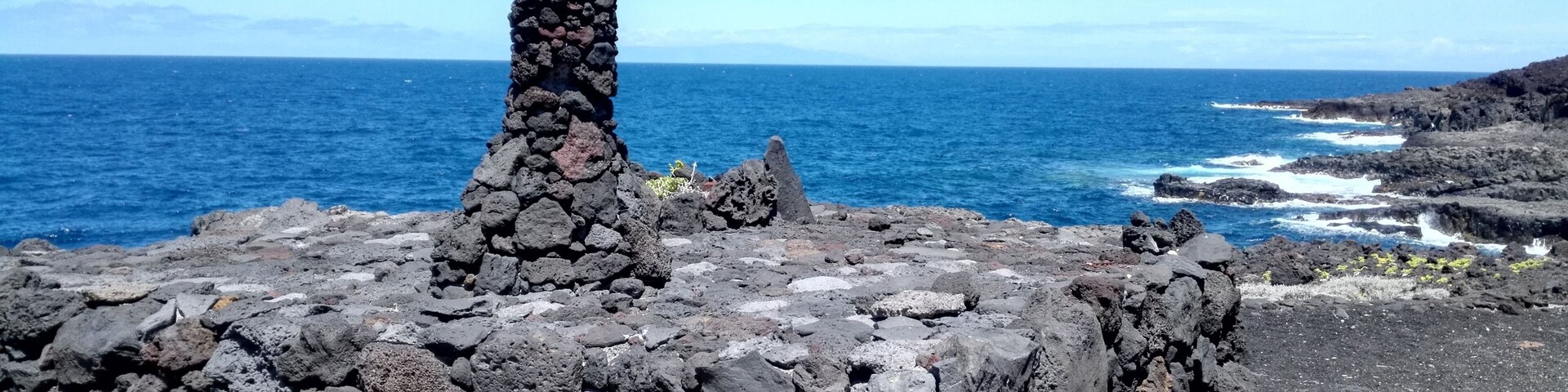 A rocky coastal landscape with a prominent stone structure and the ocean in the background.