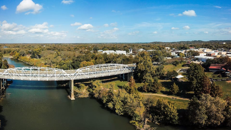 A white bridge over a river, surrounded by trees and buildings.