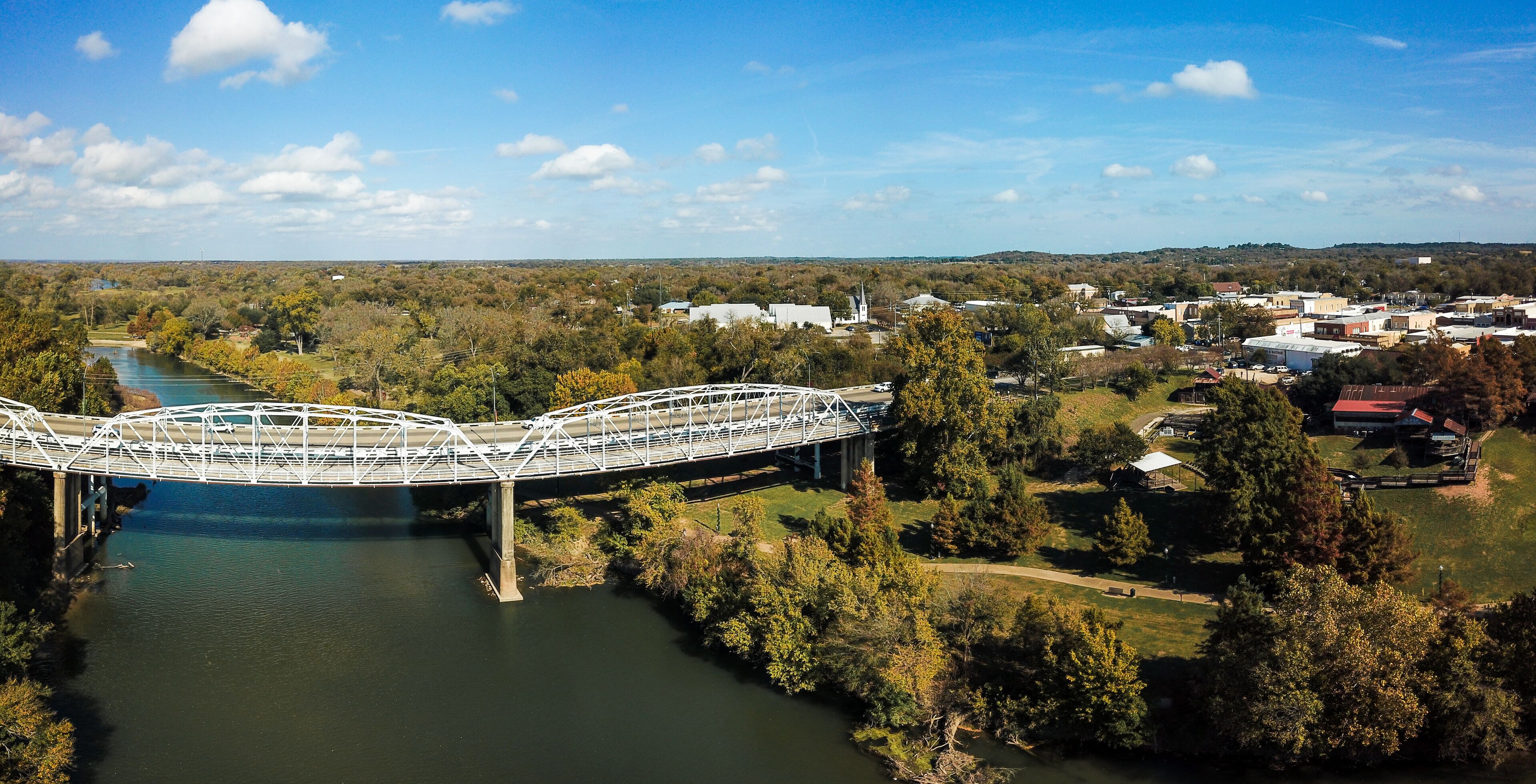 A white bridge over a river, surrounded by trees and buildings.