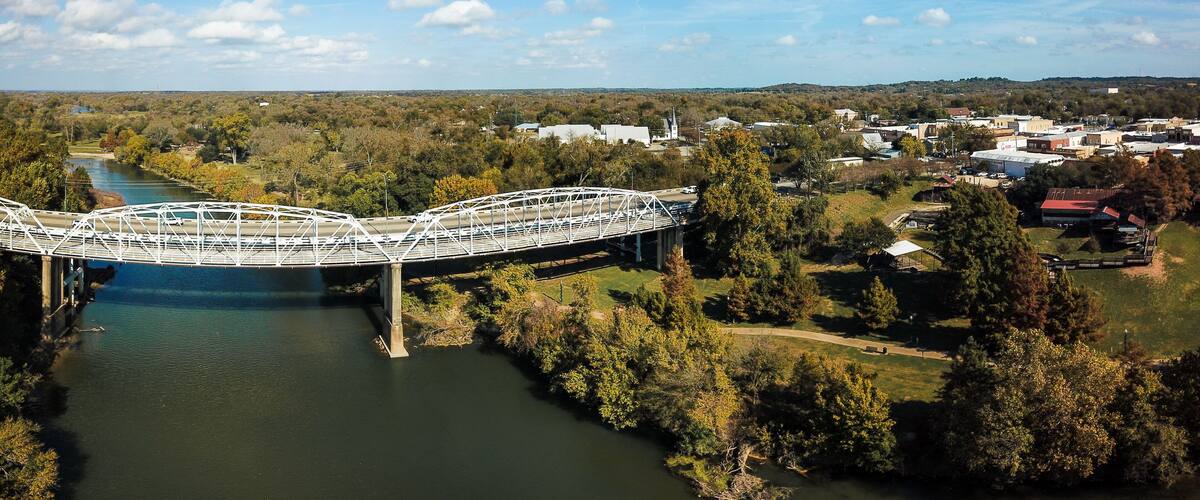 A white bridge over a river, surrounded by trees and buildings.