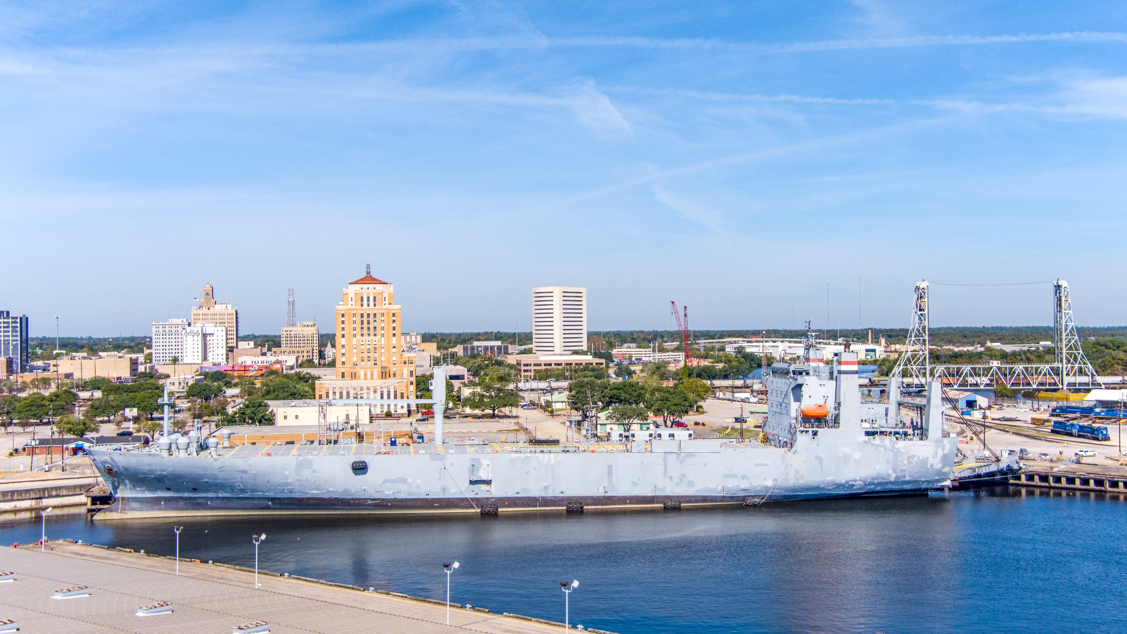 Aerial view of Beaumont Texas cityscape with modern and historic building, a large  Fuel storage tanks, the Commercial Dock and Port and oil refineries in the background with a partly cloudy blue sky.