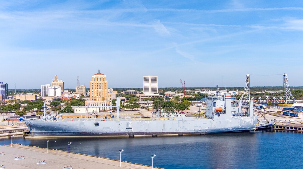 Aerial view of Beaumont Texas cityscape with modern and historic building, a large Fuel storage tanks, the Commercial Dock and Port and oil refineries in the background with a partly cloudy blue sky.