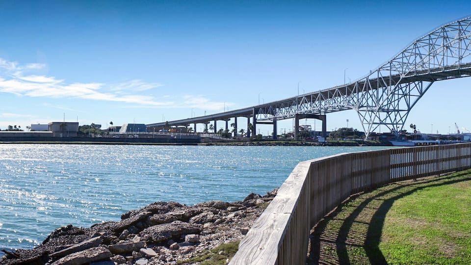 A coastal cityscape with a prominent bridge, an art museum, and a waterfront promenade.