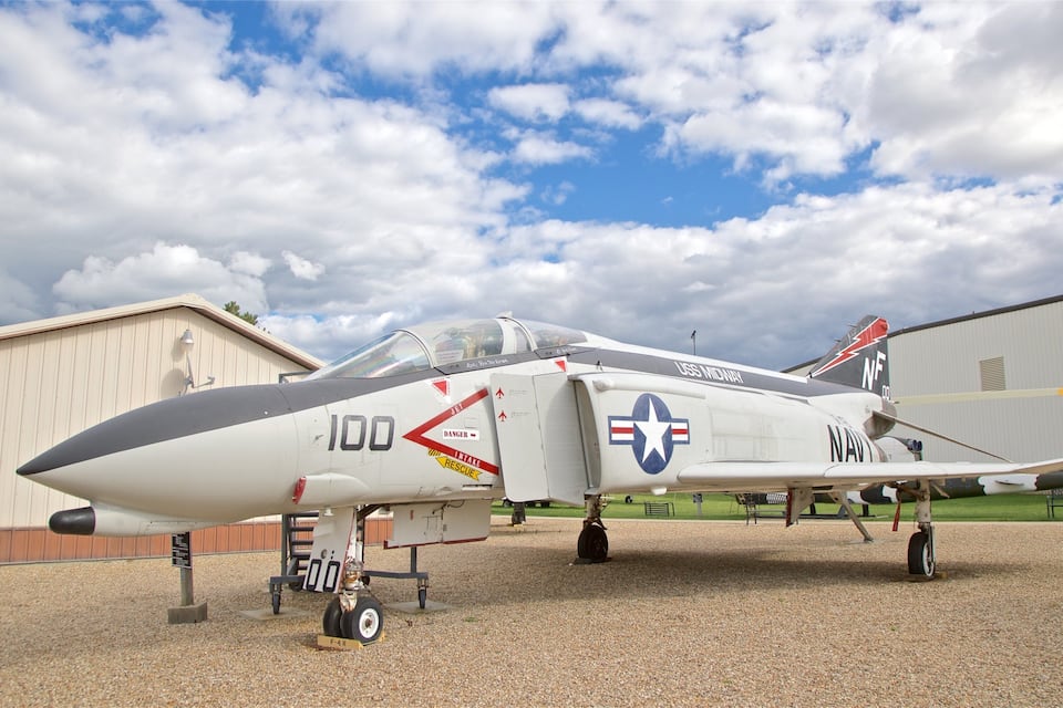 A military jet parked on a gravel surface with a building in the background.