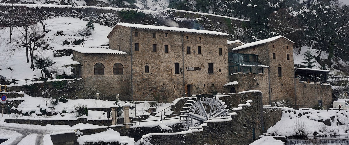 A historic stone building with a water wheel and snow-covered surroundings.