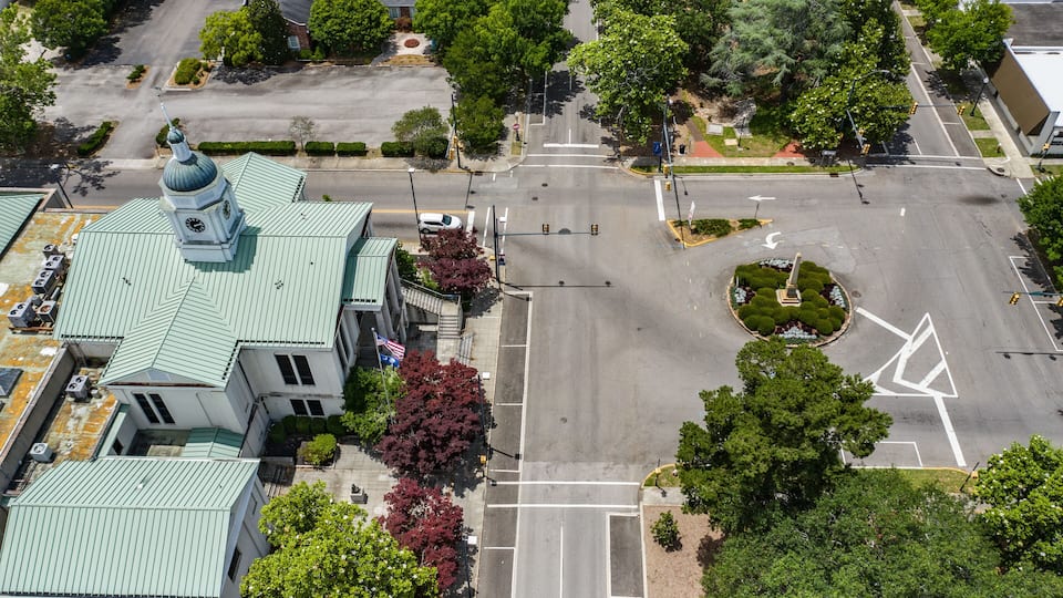 An aerial view of a city intersection with a church, trees, and a roundabout.