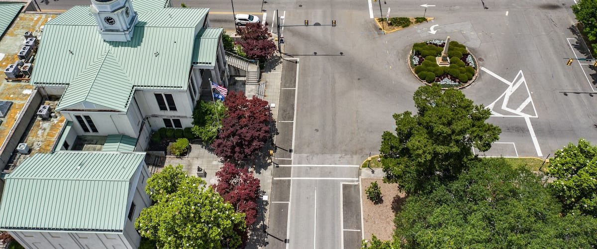 An aerial view of a city intersection with a church, trees, and a roundabout.