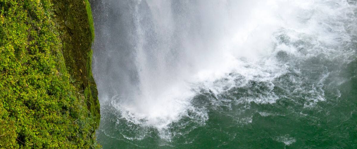A waterfall cascading down a moss-covered cliff into a turbulent river.