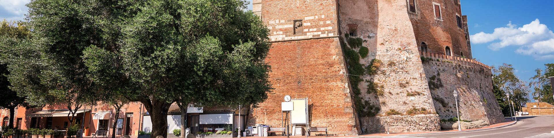 A historic brick tower with battlements, a clear blue sky, and a tree-lined street.