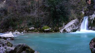 A turquoise river flowing through a forest with a waterfall.