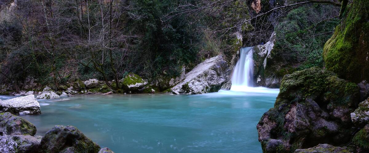 A turquoise river flowing through a forest with a waterfall.