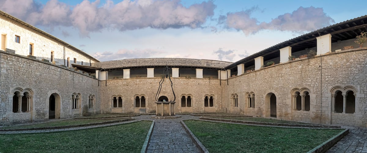 A courtyard with stone buildings, arched windows, and a central fountain.
