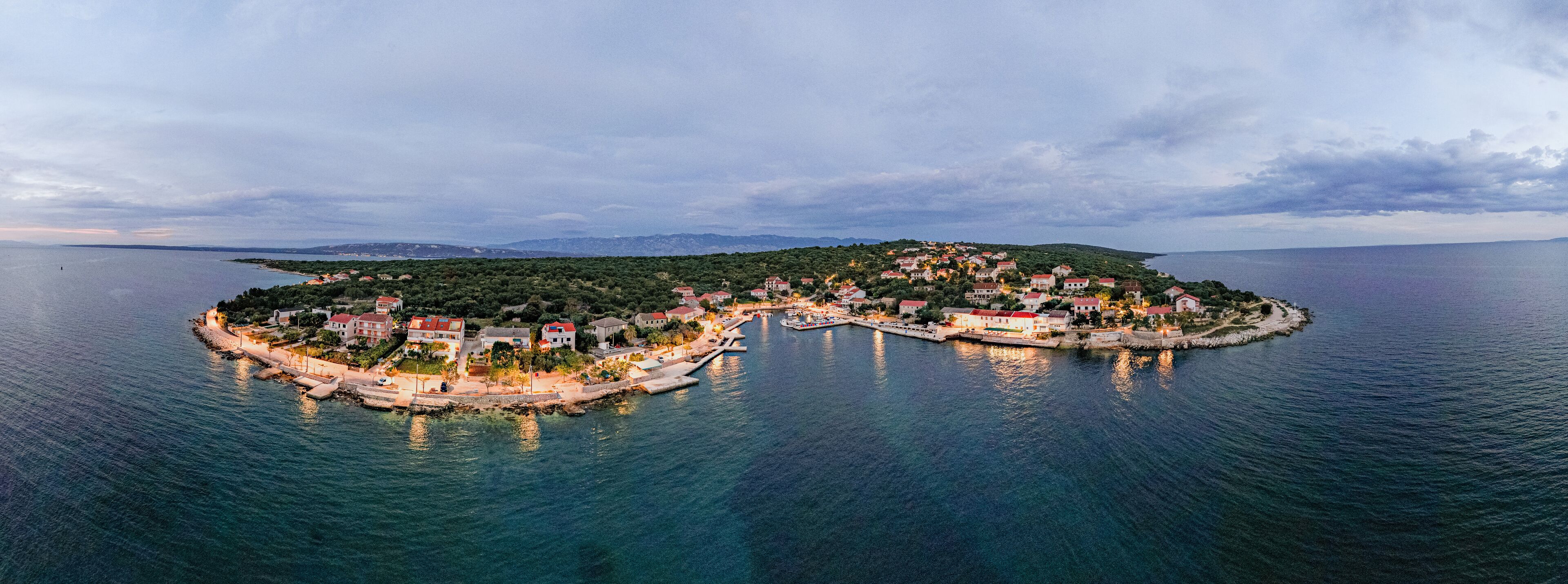 An island with a heart-shaped coastline, surrounded by calm waters and a backdrop of distant mountains.
