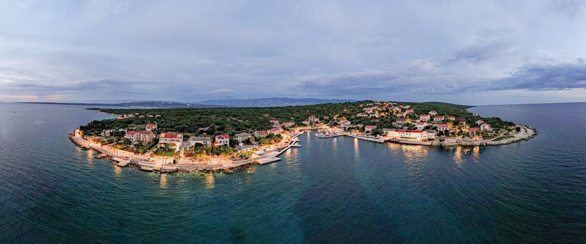 An island with a heart-shaped coastline, surrounded by calm waters and a backdrop of distant mountains.