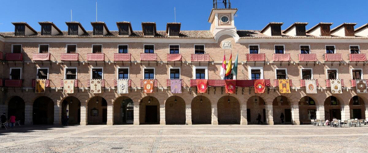 A historic building with a clock tower, arched walkways, and colorful flags.