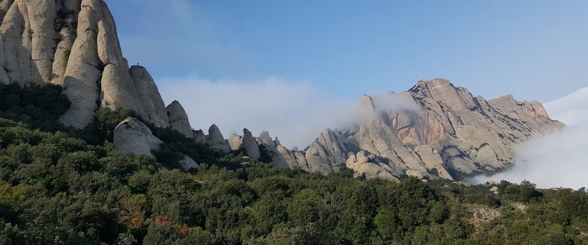 A mountainous landscape with prominent rock formations and a dense forest at the base.