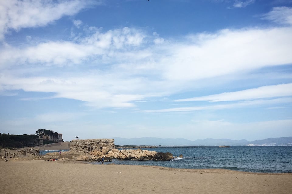 A beach with a rocky outcrop and a building in the background.