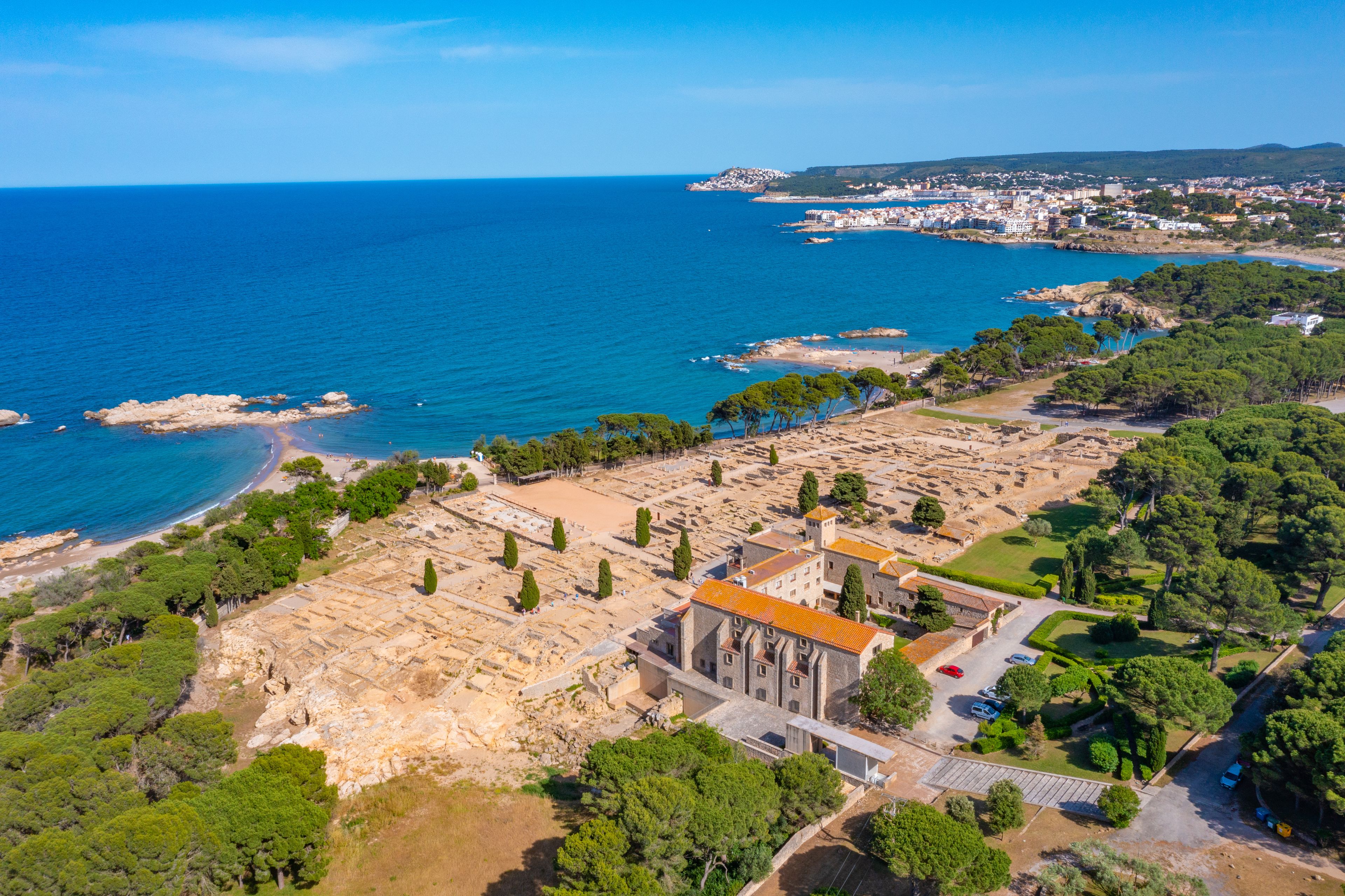 An aerial view of a coastal town with a historic building, clear blue sea, and surrounding greenery.