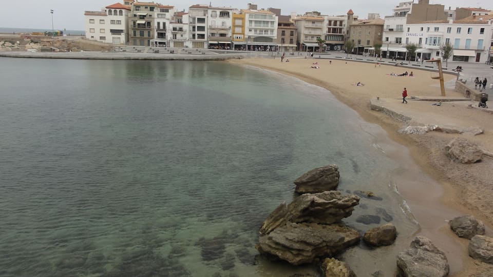 A coastal town with a sandy beach, clear water, and rocky outcrops.