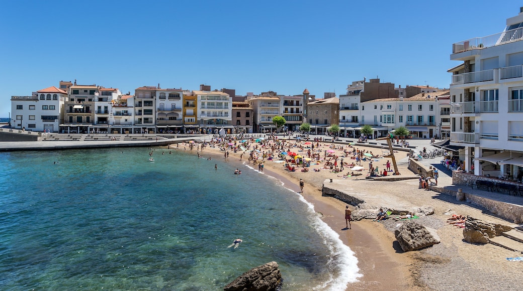 A crowded beach with clear blue water, a rocky shoreline, and buildings along the coast.