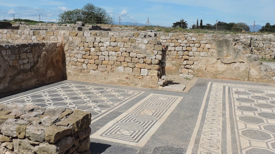 Ancient ruins with stone walls and patterned mosaic floors.