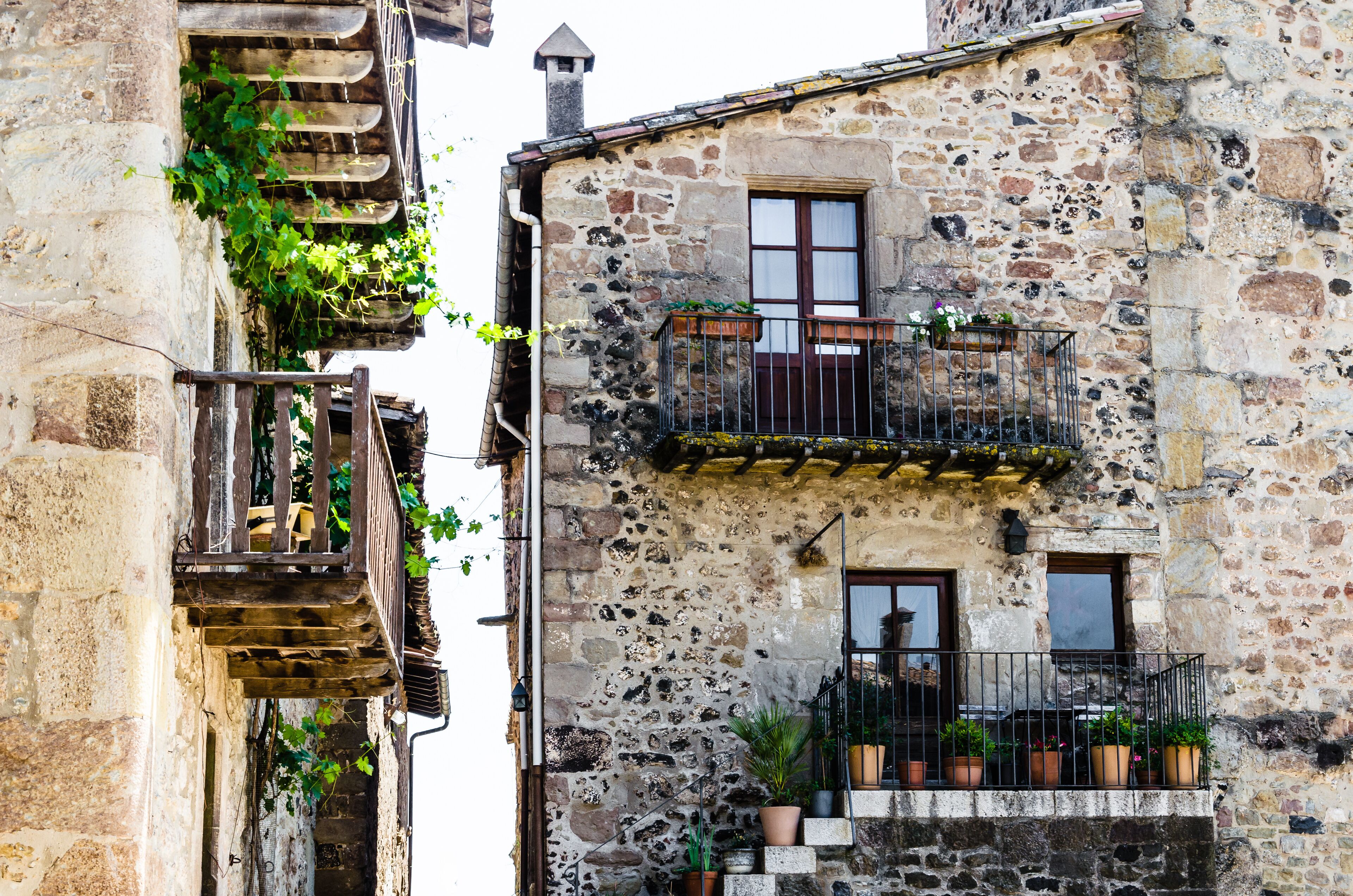 A stone building with a wooden staircase, balconies with potted plants, and a chimney.
