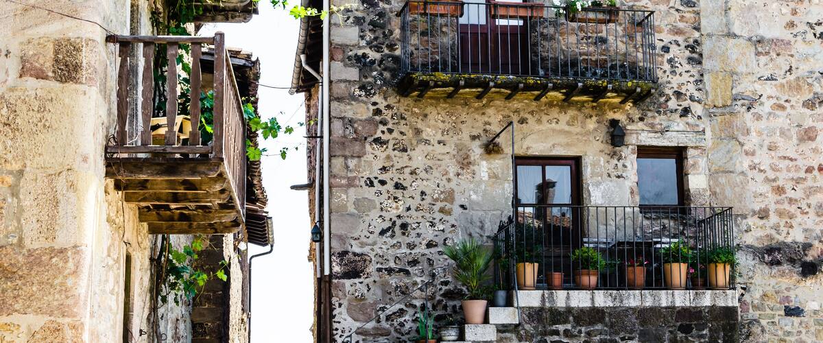 A stone building with a wooden staircase, balconies with potted plants, and a chimney.
