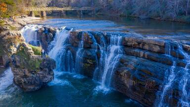Scenic High Falls Park waterfall in North Alabama with hikers on cliff edge and pedestrian bridge in background