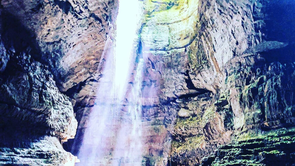 Eine Person steht auf einer Felsformation, während ein Wasserfall eine Klippe hinabstürzt.