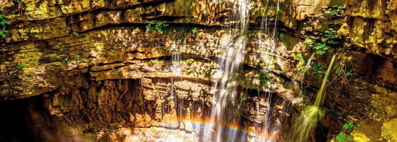 Una cascada fluye sobre un acantilado rocoso rodeado de abundante vegetación.