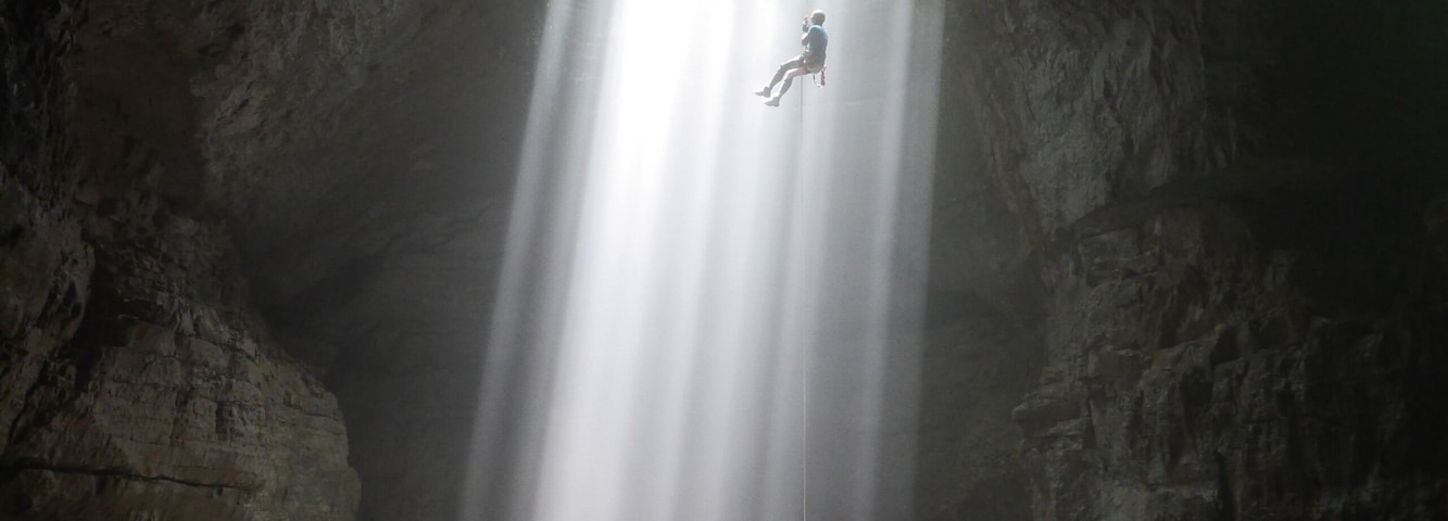Uma pessoa rapelando em uma cachoeira dentro de uma caverna.