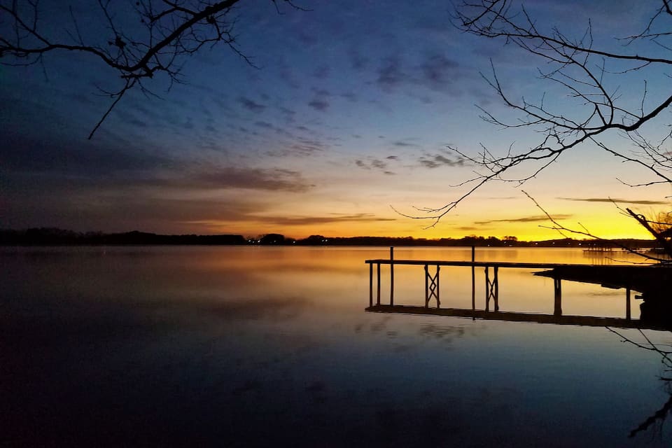 A calm lake at sunset with a dock extending into the water.