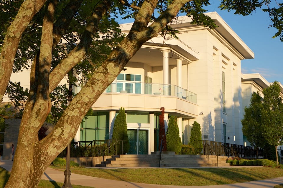 A modern building with a white facade, large windows, and a central staircase leading to a balcony.