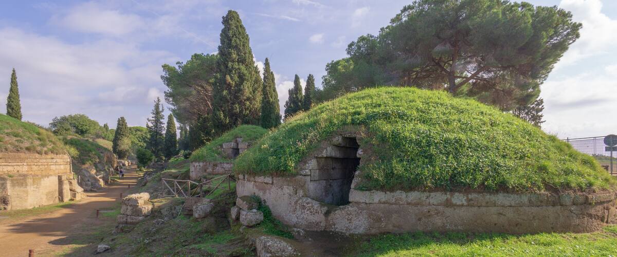 Ancient stone structures with grass-covered roofs, a dirt path, and surrounding trees.